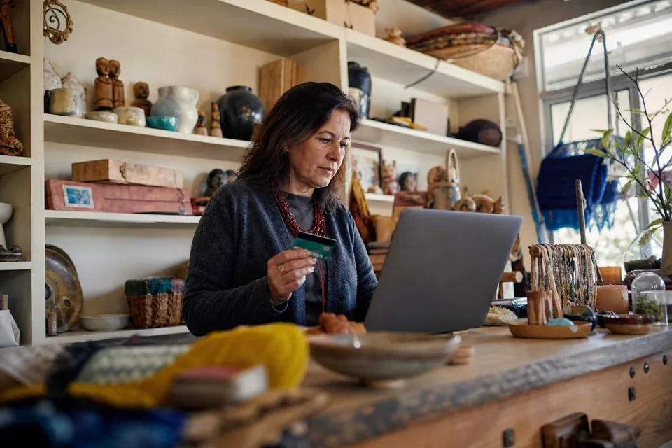 Shop owner with a payment card in hand looking at a laptop on the shop counter