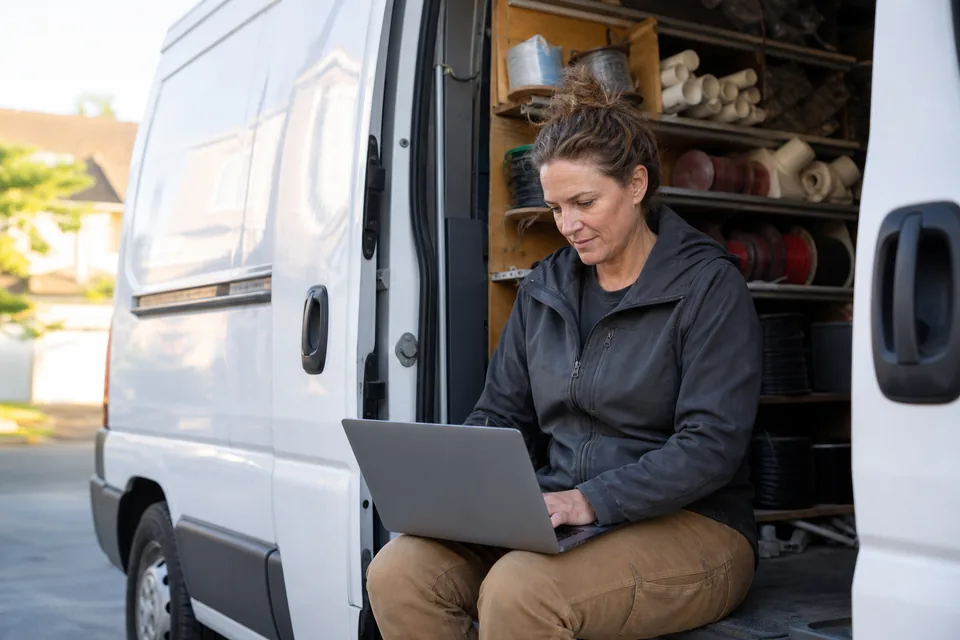Owner of an electrical contracting company reviewing her website on a laptop in the back of a work van