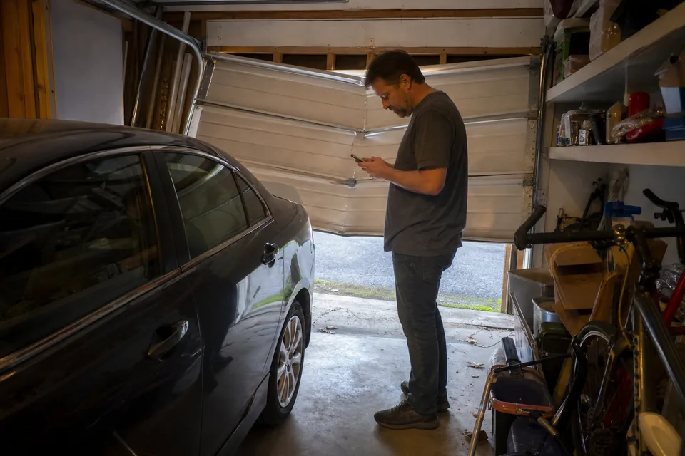 Homeowner in a garage looking at a stuck garage door while searching on a phone