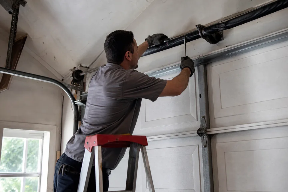 Garage door technician on a ladder working on a torsion spring above a garage door